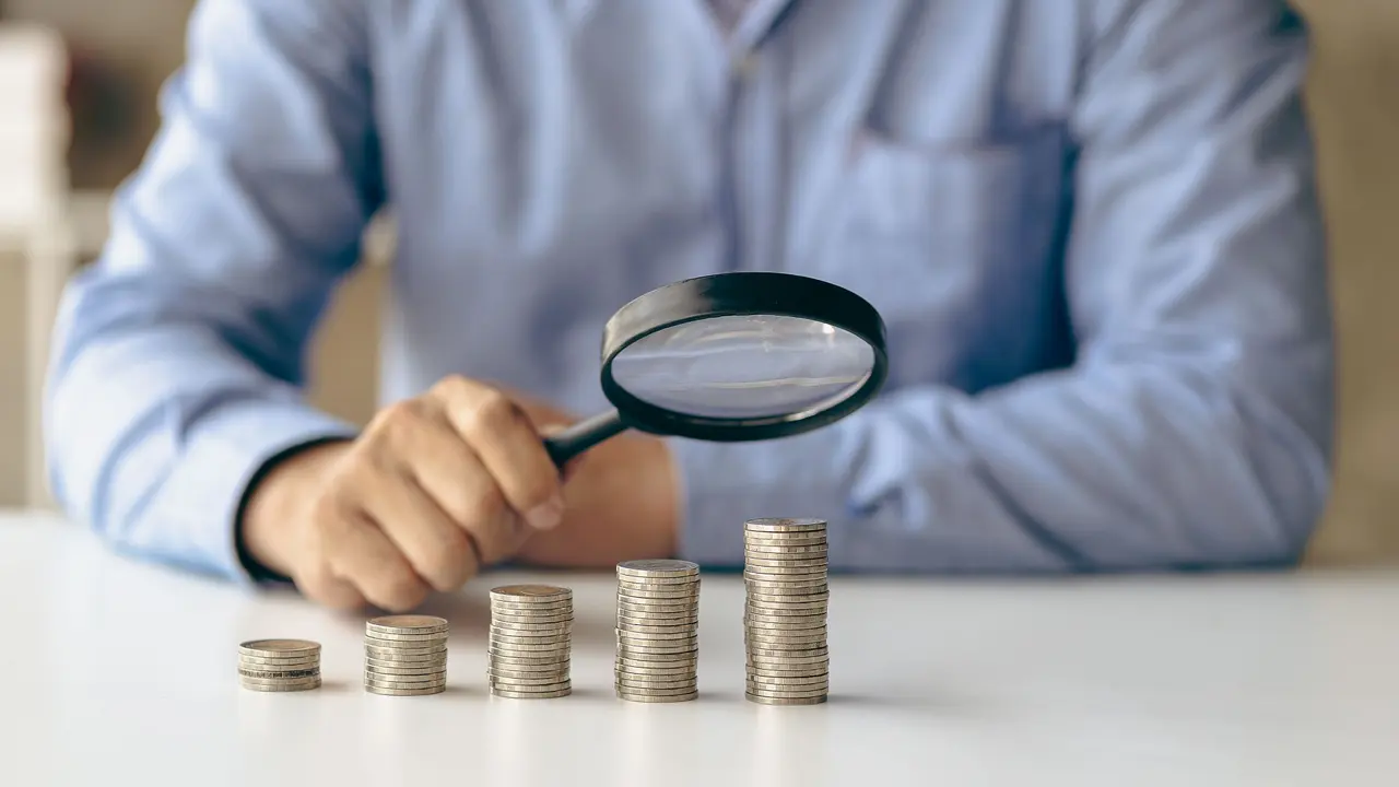 Close up of businessman holding magnifying glass over coins and money looking at something on coins stacked on table, financial business concept stock photo